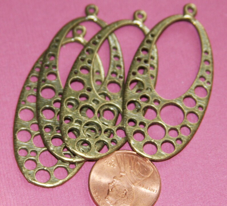 May include: Four antique brass oval-shaped earring blanks with a decorative circle pattern. The blanks have a hole at the top for attaching earring hooks.