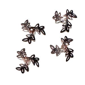 May include: Four identical metal bead caps with an antique bronze finish, each featuring a three-pronged design with intricate cut-out leaf patterns radiating from a central circular opening, arranged in a scattered formation on a white background.
