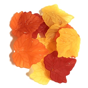 Puede incluir: Una colección de pequeñas cuentas translúcidas con forma de hoja en colores otoñales, incluyendo naranja vibrante, rojo intenso y amarillo brillante. Cada cuenta presenta un patrón de venas detallado y un pequeño orificio.