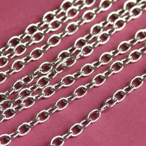 May include: Close-up of multiple silver chains with oval links. The chains are arranged in a staggered pattern on a pink surface.