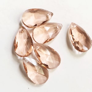May include: Six teardrop-shaped crystal prisms in a light peach color. The prisms have a faceted design and a hole at the top for hanging.