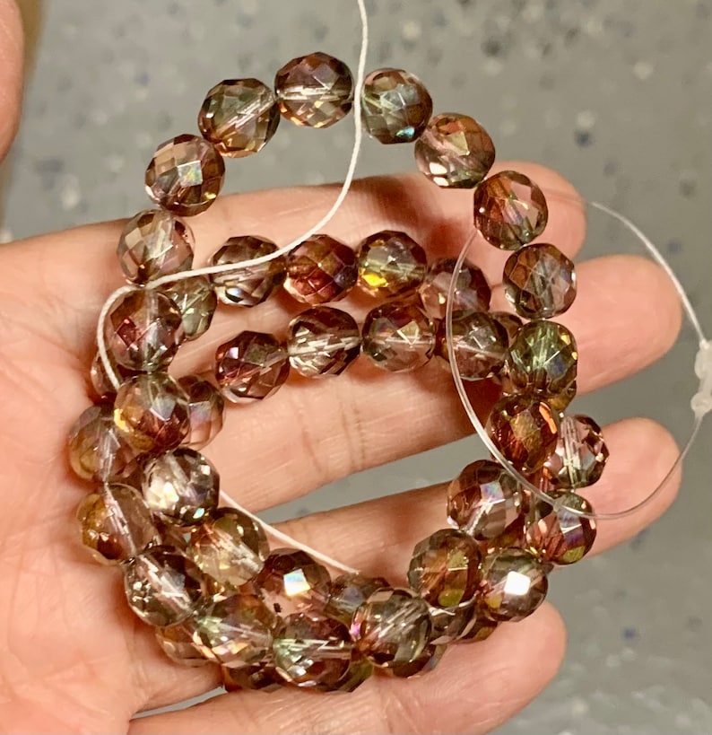 May include: A strand of iridescent glass beads in shades of brown, green, and gold. The beads are faceted and have a shimmering effect.
