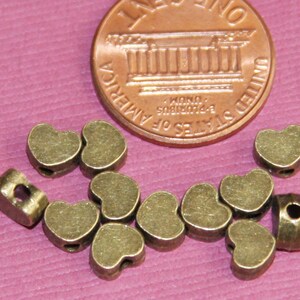 May include: A group of 10 antique gold heart-shaped metal beads with a hole in the centre. The beads are about the size of a UK penny.