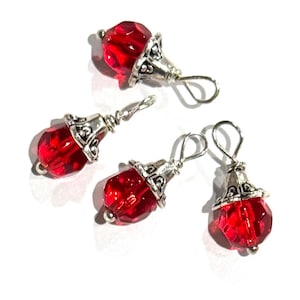 May include: Four faceted red crystal beads, each topped with a decorative silver-toned metal cap and a small wire loop for hanging. The beads are translucent and catch the light, featuring a classic teardrop shape with intricate metal detailing.
