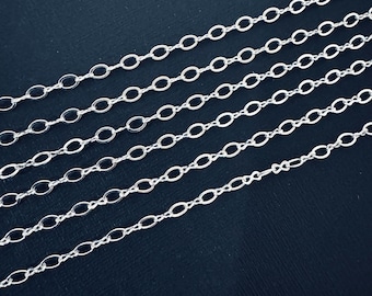 May include: Close-up of several strands of delicate silver-colored chain. The chains are composed of small, oval links, creating a repeating pattern. The chains are arranged diagonally against a dark background, highlighting their reflective quality.
