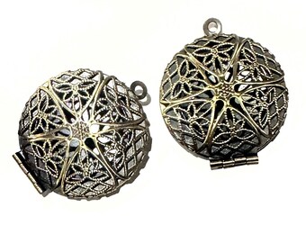 May include: Two gold-toned metal cage pendants with intricate floral designs. The pendants are open on one side and have a hinged closure.