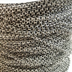 May include: A close-up of a silver chain, coiled and ready for use in jewelry making. The chain is made of small, linked circles, creating a delicate and versatile look.
