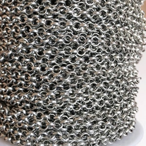 May include: A close-up of a silver chain, coiled and ready for use in jewelry making. The chain is made of small, linked oval shapes.