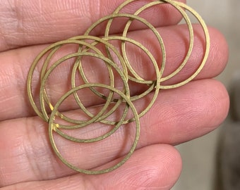 May include: A group of eight gold-coloured metal jump rings, all different sizes, are stacked on top of each other. The rings are smooth and shiny.