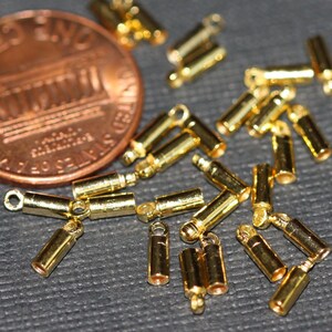 Puede incluir: Primer plano de un grupo de tapones de metal dorados para la fabricaci&oacute;n de joyas. Los tapones tienen un peque&ntilde;o bucle en un extremo y una superficie plana en el otro extremo.