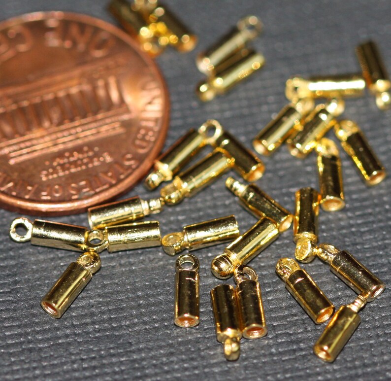 Puede incluir: Primer plano de un grupo de tapones de metal dorados para la fabricaci&oacute;n de joyas. Los tapones tienen un peque&ntilde;o bucle en un extremo y una superficie plana en el otro extremo.