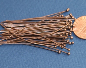 Puede incluir: Un conjunto de alfileres de cabeza de color cobre, cada uno con una pequeña bola en el extremo. Los alfileres están dispersos sobre una superficie azul junto a una moneda para comparar el tamaño. Ideales para la fabricación de joyas y manualidades.
