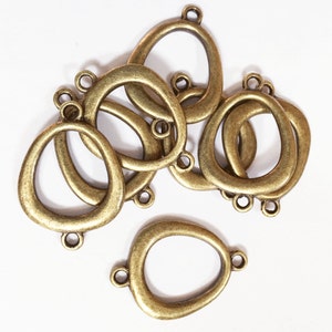 May include: A group of six antique gold-toned metal oval-shaped pendant connectors with a smooth, slightly irregular surface. Each connector has two small loops on the top and one on the bottom.