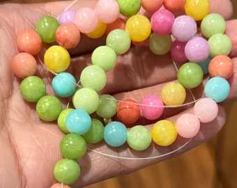 Puede incluir: Una hebra de cuentas redondas de colores pastel, incluyendo tonos de verde, rosa, amarillo y azul. Las cuentas están enhebradas en un cordón elástico transparente.