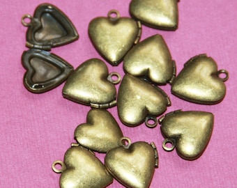 May include: A collection of ten gold-toned heart-shaped locket charms. The lockets are open and closed, revealing a small space inside. The lockets are arranged on a pink background.
