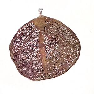 May include: A delicate, brown, leaf-shaped pendant with a intricate, lacy pattern of holes throughout. The pendant has a slightly rounded, oval shape and a small loop at the top for hanging.