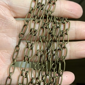 Puede incluir: Primer plano de varios hilos de cadena de color dorado, con un diseño ovalado enlazado. La cadena se sostiene en una mano, mostrando los intrincados detalles del metal.