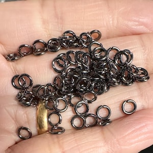 May include: A large pile of black jump rings. The rings are small and round, and they are all made of metal.