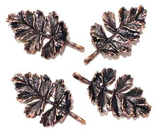 May include: Four metal leaf charms with a dark copper finish and a textured, veined surface. Each charm features a detailed botanical design with multiple small, serrated leaflets and a small loop at the stem for attachment to jewelry or crafts.