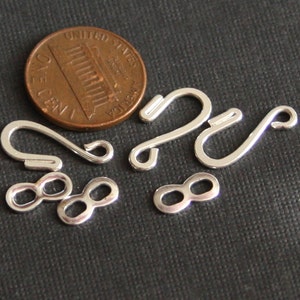 Op de afbeelding: Zilverkleurige sieraden sluitingen en connectoren, waaronder twee oneindigheidssymbolen, twee karabijnhaken en een haaksluiting. De sluitingen worden getoond naast een Amerikaanse penny voor schaal.