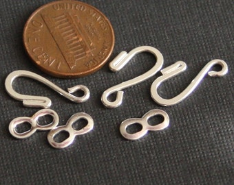 May include: Silver-toned jewelry clasps and connectors, including two infinity symbols, two lobster claw clasps, and one hook clasp. The clasps are shown next to a US penny for scale.