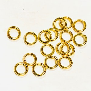 May include: A pile of gold jump rings, a type of jewellery finding used for connecting chains, cords, and other jewellery components.