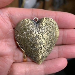K&ouml;nnte beinhalten: Ein goldfarbenes herzf&ouml;rmiges Medaillon mit einem komplizierten floralen Design.