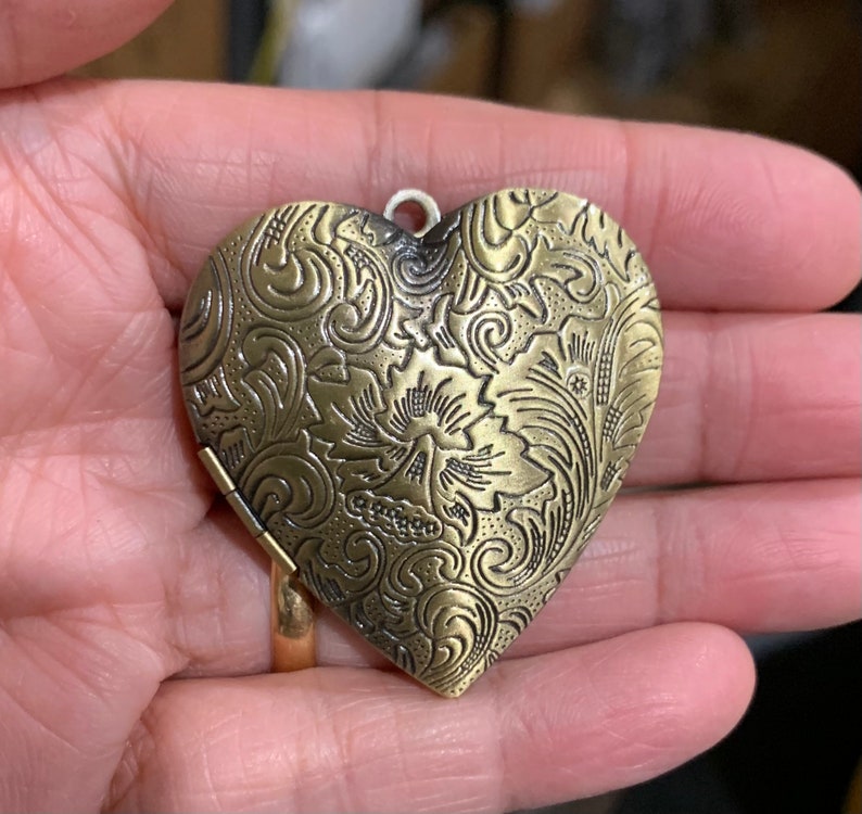 K&ouml;nnte beinhalten: Ein goldfarbenes herzf&ouml;rmiges Medaillon mit einem komplizierten floralen Design.