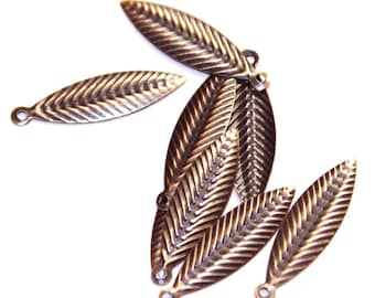 May include: A collection of six antique bronze-toned metal leaf charms, each featuring a detailed herringbone texture and a small circular loop at one end for attachment. The charms are arranged in a scattered, overlapping pattern against a white background.