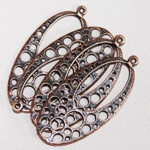 May include: Three antique copper oval-shaped metal charms with a decorative cutout design. The charms have a textured surface and a loop at the top for attaching to jewelry or other crafts.