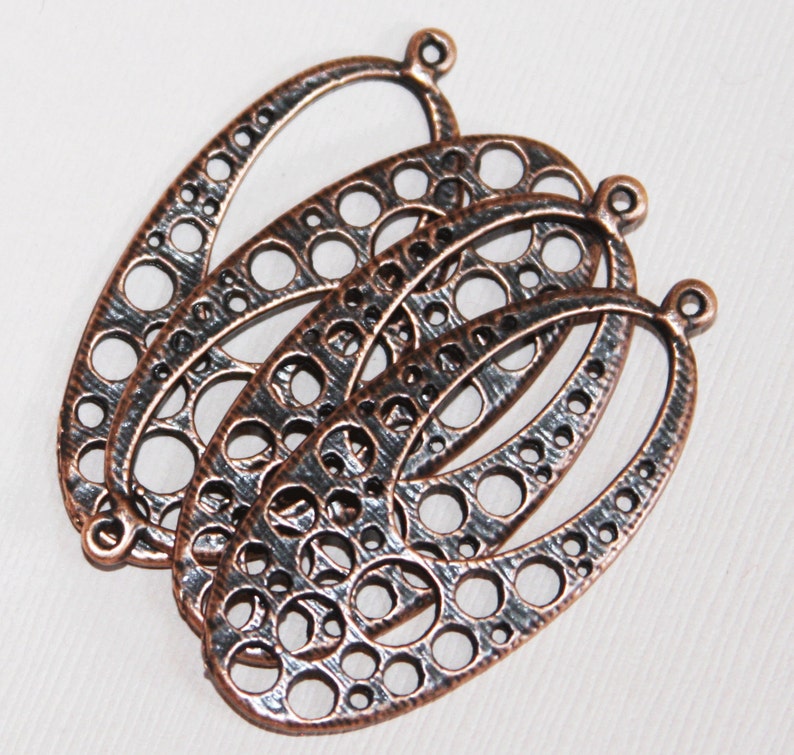 May include: Three antique copper oval-shaped metal charms with a decorative cutout design. The charms have a textured surface and a loop at the top for attaching to jewelry or other crafts.