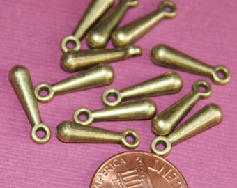 May include: A group of ten antique gold-toned metal teardrop-shaped charms with a loop at the top. The charms are scattered on a pink surface.