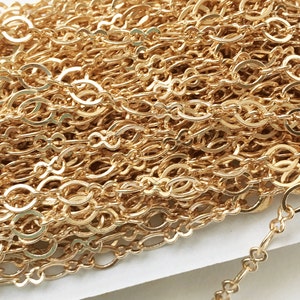 May include: A close-up of a gold chain with a delicate, oval-shaped link pattern. The chain is coiled and arranged in a pile, showcasing the intricate design.
