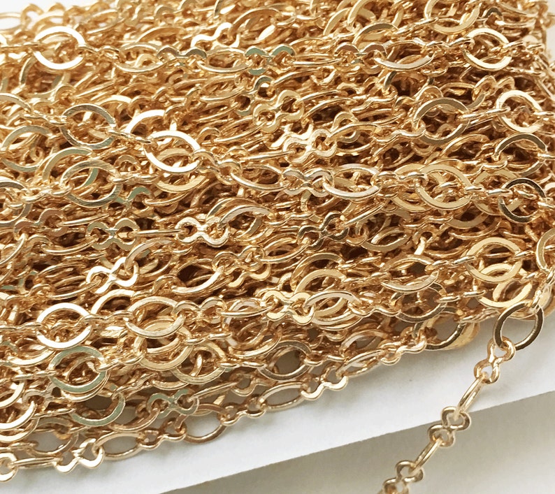 May include: A close-up of a gold chain with a delicate, oval-shaped link pattern. The chain is coiled and arranged in a pile, showcasing the intricate design.