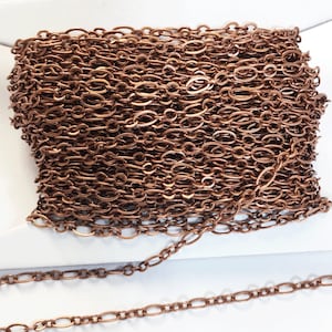 May include: A spool of copper chain, the chain is made of oval links. The chain is coiled and a small section is uncoiled to show the detail of the chain.