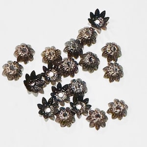 May include: A collection of silver-toned metal flower-shaped bead caps. The caps have a small hole in the center and are designed to be used for jewelry making.