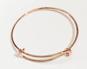 May include: A rose gold expandable bangle bracelet with a knotted closure.