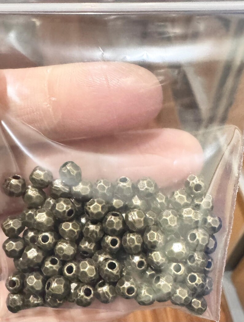 Pu&ograve; includere: Un sacchetto di perline in metallo dorato antico. Le perline sono rotonde e hanno un design sfaccettato.