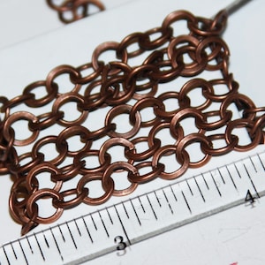 Puede incluir: Primer plano de una cadena de cobre con una regla que muestra 3 y 4 pulgadas. La cadena está hecha de pequeños círculos unidos.