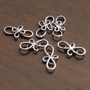 Op de afbeelding: Zes zilveren metalen decoratieve versieringen in de vorm van een gestileerde bloem met een lusontwerp.