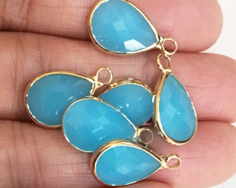 May include: Five turquoise blue teardrop-shaped glass beads with gold-toned metal accents and jump rings. The beads are approximately 1 inch in length.