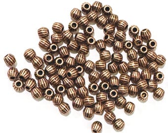 Könnte beinhalten: Eine Ansammlung kleiner, runder, kupferfarbener Metallperlen mit vertikaler Rippenstruktur. Jede Perle hat ein mittiges Loch zum Auffädeln. Die Perlen liegen in einem losen Haufen und weisen eine einheitliche metallische Oberfläche auf.