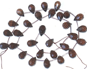 May include: A strand of brown faceted gemstone beads in a teardrop shape. The beads are strung on clear thread and are approximately 18mm in length.