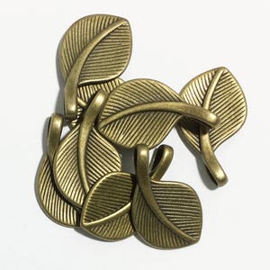 May include: A set of six antique gold leaf-shaped metal charms with a textured surface. The charms have a loop at the top for attaching to jewelry or other crafts.