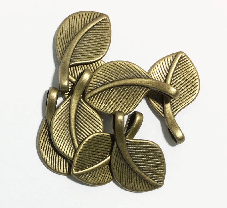 May include: A set of six antique gold leaf-shaped metal charms with a textured surface. The charms have a loop at the top for attaching to jewelry or other crafts.