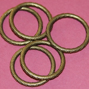 May include: Four gold-colored metal rings with a textured surface. The rings are stacked on top of each other.