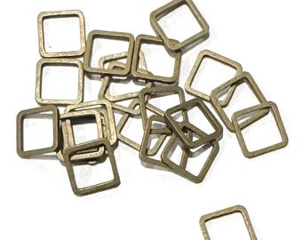 May include: A pile of gold-toned metal jump rings, each shaped like a square. The rings are scattered on a white surface.