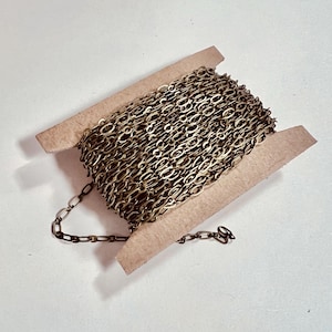 May include: A spool of gold-toned chain, wound around a cardboard spool. The chain is made of oval links.