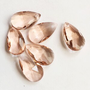 May include: Six teardrop-shaped crystal prisms in a light peach color. The prisms have a faceted design and a hole at the top for hanging.