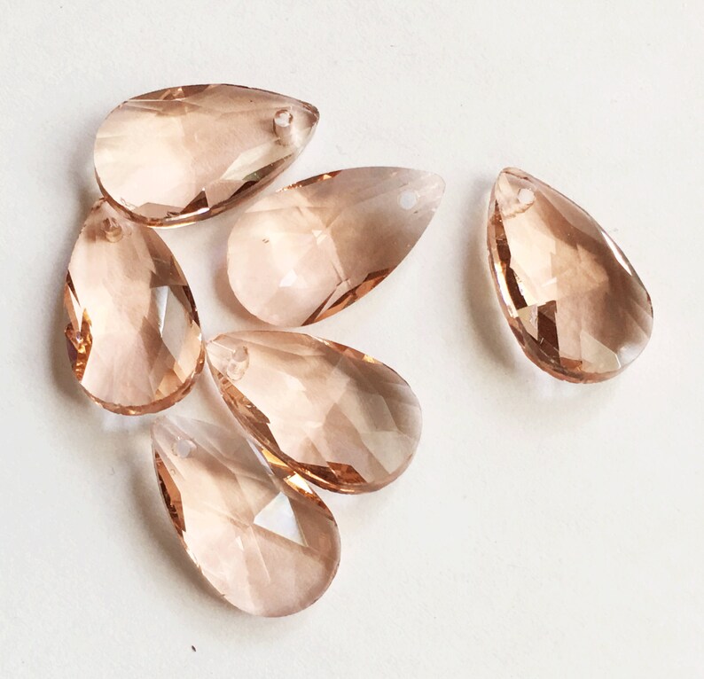 May include: Six teardrop-shaped crystal prisms in a light peach color. The prisms have a faceted design and a hole at the top for hanging.